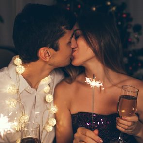 Christmas and New year party concept. Couple kissing, burning sparklers by illuminated Christmas tree with champagne.