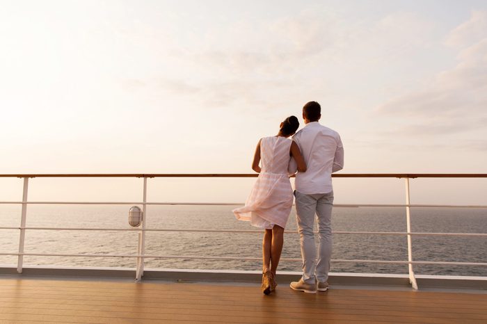 rear view of young couple standing on ship deck during sunset