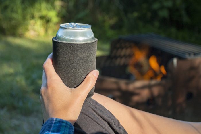 Woman holding a can of beer in a sleeve by the fire while camping