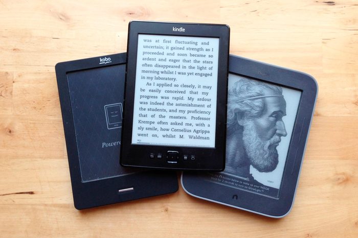 A collection of ebook ereaders, including a Kobo, a Barnes and Noble NOOK and an Amazon Kindle sit on a wooden bench