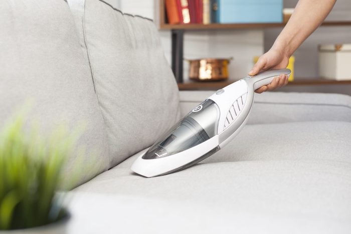 Woman with handheld vacuum cleaning on sofa; Shutterstock ID 511880752