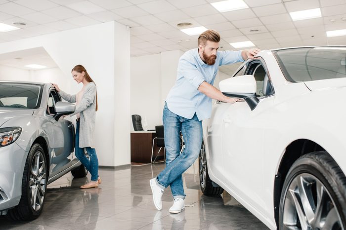 Couple choosing car, man and woman looking on various cars in dealership salon 