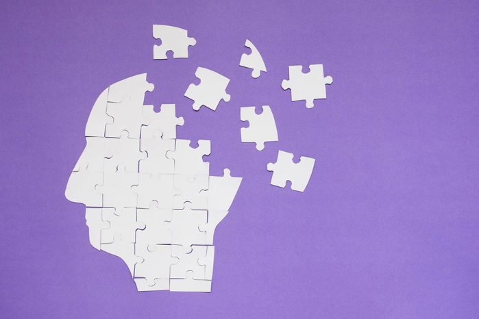 White jigsaw puzzle as a human brain on purple background w/ copy space. Creative idea for memory loss, Alzheimer's disease, dementia, Parkinson's disease, emotion stress and mental health concept.