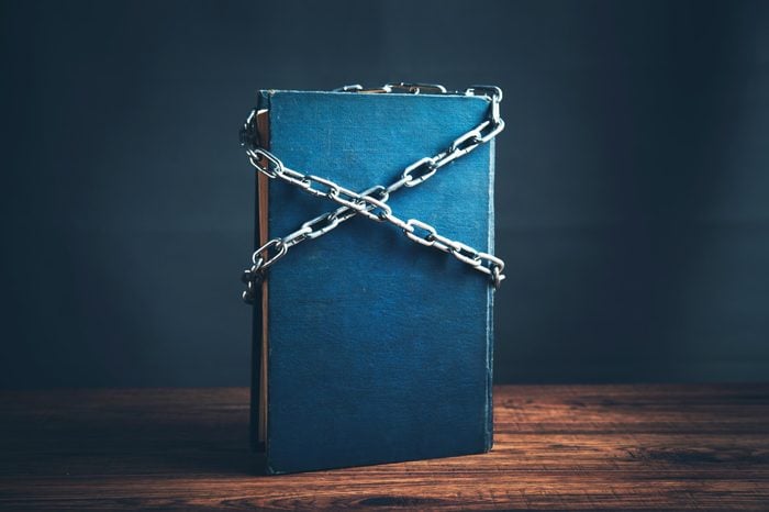 single blue book standing up on wood table with chains crossed across the cover