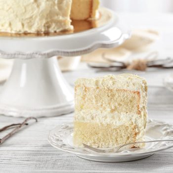 Slice of delicious vanilla cake on wooden table