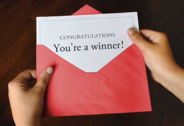 An open red envelope with a letter that says Congratulations You're a winner! with female hands holding it up