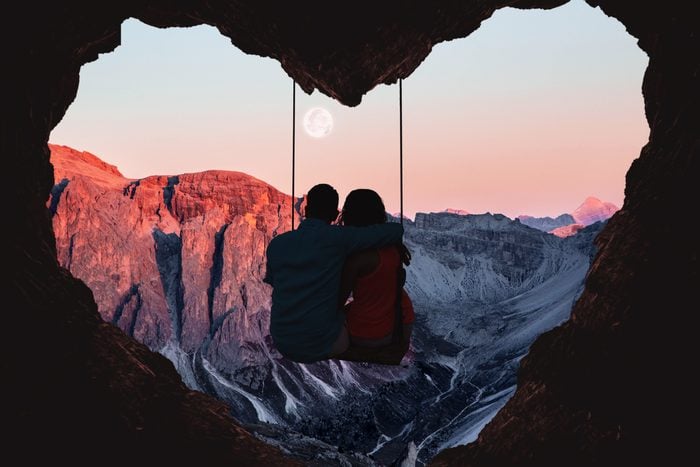 A couple sitting on a swing in front of a heart cave at sunset