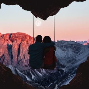 A couple sitting on a swing in front of a heart cave at sunset