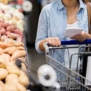 An unrecognizable woman pushes her cart past the potatoes in the grocery store.