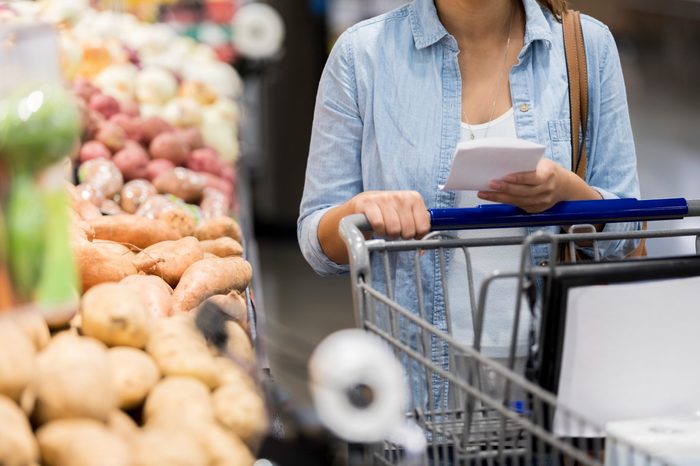 An unrecognizable woman pushes her cart past the potatoes in the grocery store.