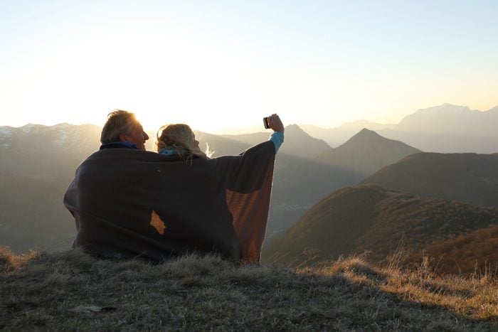 Couple wrapped in blanket taking a photo while on a scenic hike