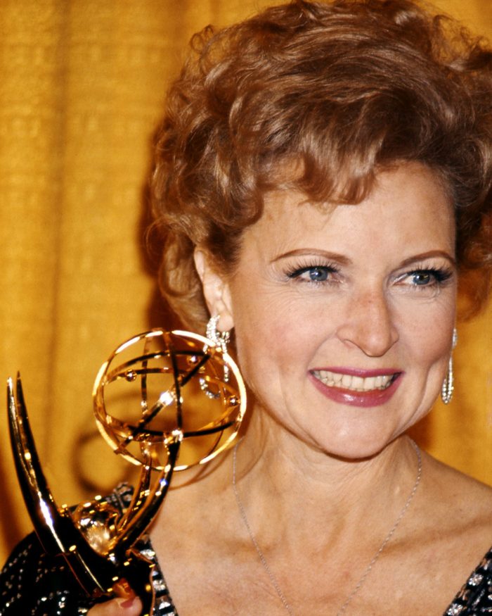 Betty White, US actress, smiling as she holds an Emmy Award, against a yellow background, USA, circa 1975.