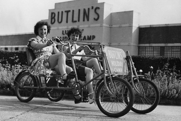 Two holidaymakers riding a bicycle for two at Butlin's Holiday Camp in Clacton