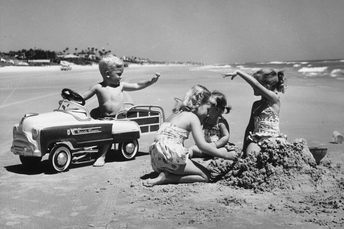 circa 1960: A young boy trying to impress three girls in his pedal car on Daytona Beach, Florida
