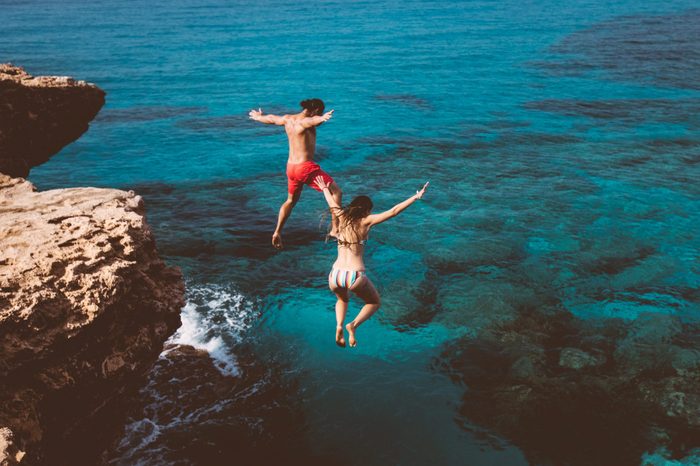 couple jumping off a cliff into the ocean on vacation
