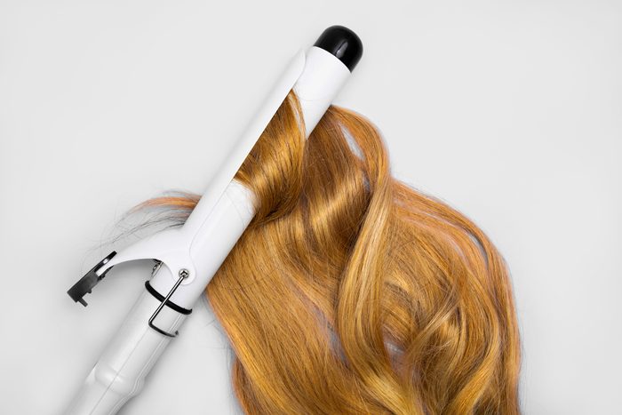 cordless curling iron with blond hair on a grey background