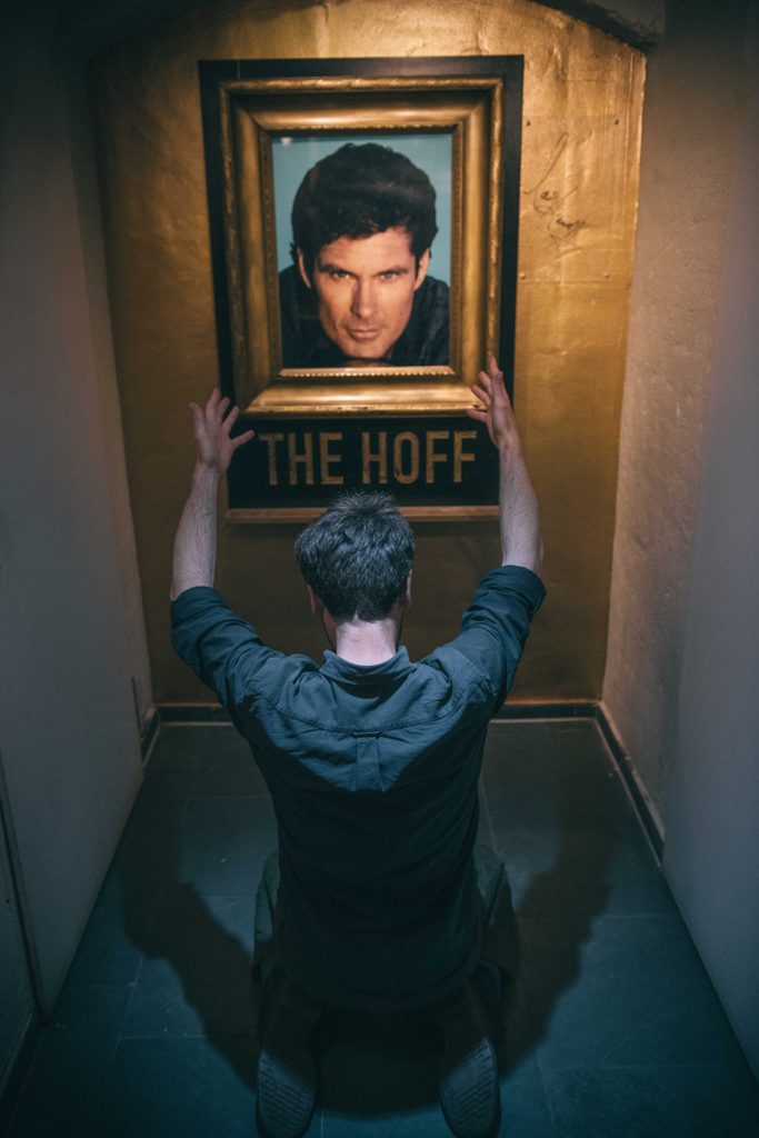 a man on his knees worships a framed image of david hasselhoff