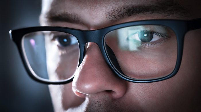 Glasses with light reflected from computer or smartphone screen. Thoughtful business man or focused student working late at night. Coder, programmer or geek with phone or laptop. Reflection of monitor