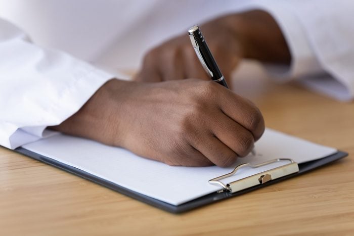 African American doctor writing on paper close up, filling patient form, document, medical history or anamnesis, sitting at desk, disease prevention, healthcare, health insurance contract