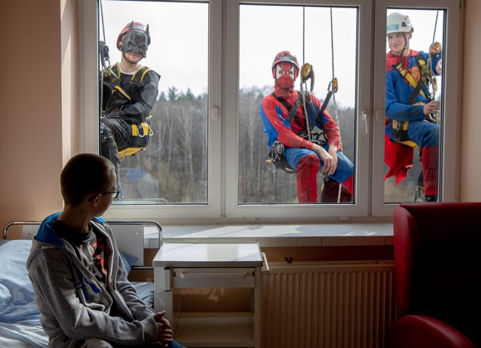 a boy looks outside his hospital window at the window washers dressed as superheros
