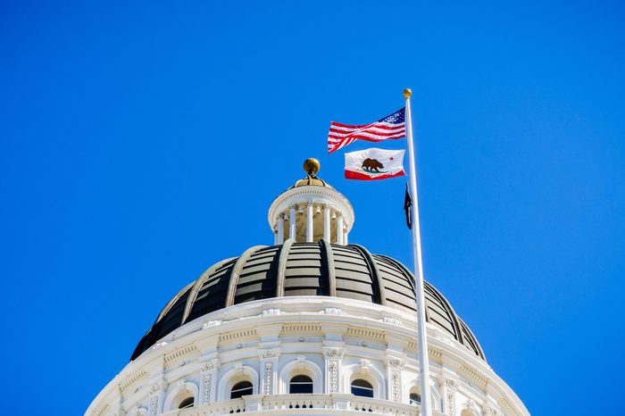 The US and the California state flag waving in the wind in front of the dome of the California State Capitol