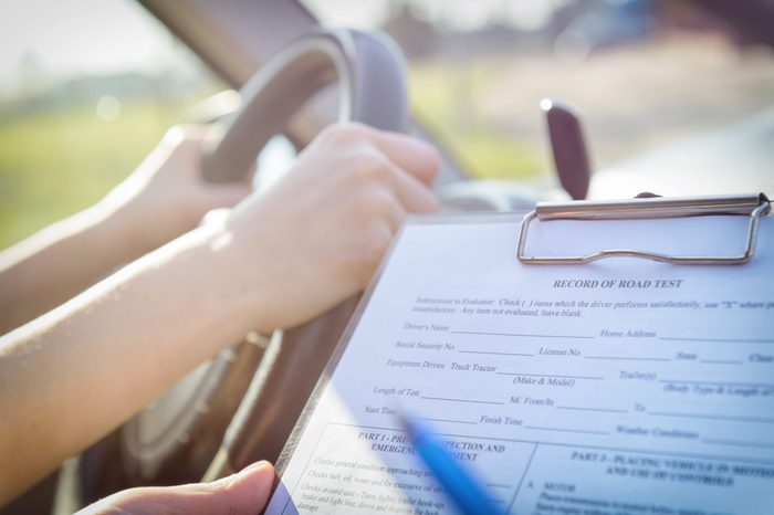 Examiner filling in driver's license road test form sitting with her student inside a car