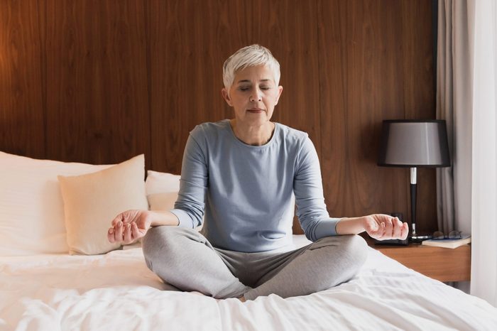 Beautiful senior woman doing yoga in her bedroom, Healthy morning routine and meditation concept