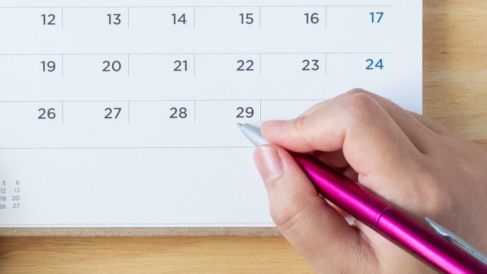 hand holding pen to a calendar on the table.