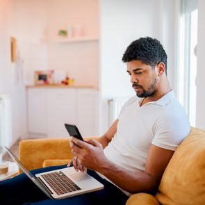 Young man sitting on sofa with laptop and mobile phone.