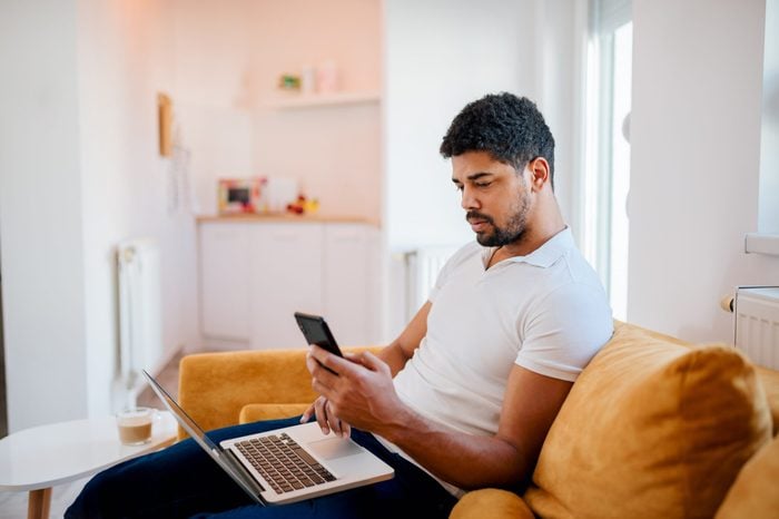 Young man sitting on sofa with laptop and mobile phone.