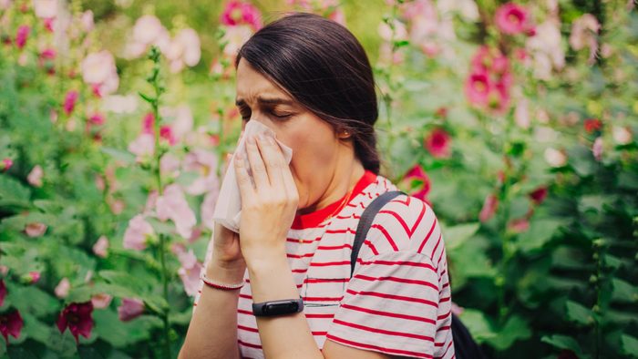 woman sneezing with a tissue outside. blurred flowers background.