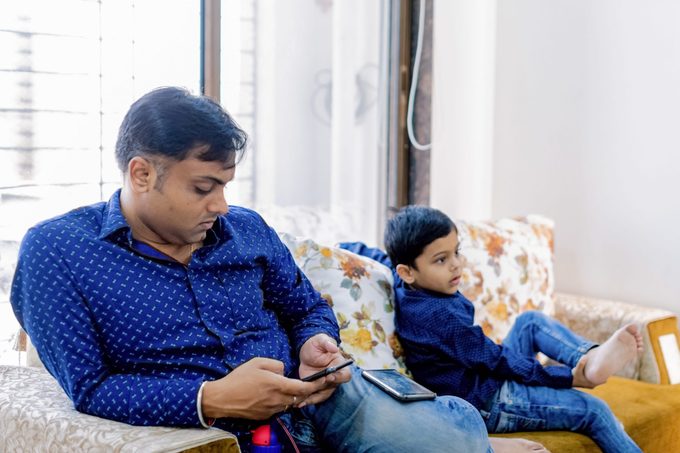 Father busy looking at his phone next to his son on the couch