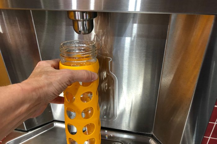 Yellow reusable glass water bottle being held under a water refill station spout