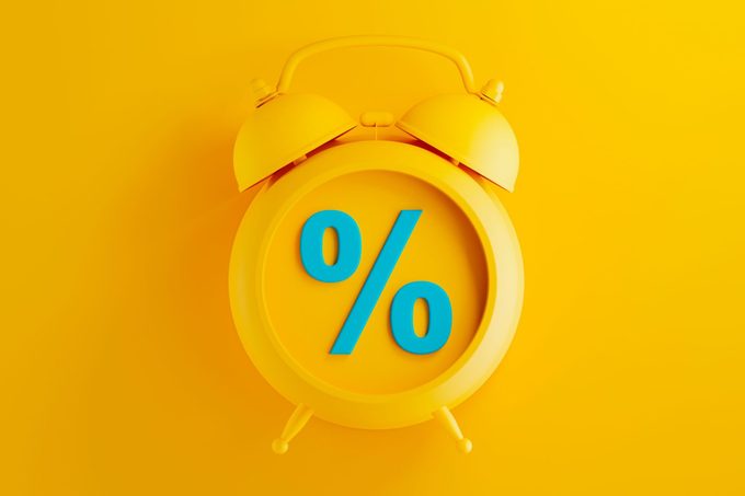 yellow alarm clock on yellow background with blue percent symbol