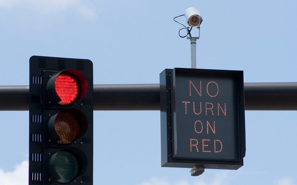 Red traffic light camera with "No Turn On Red" sign and intersection camera.