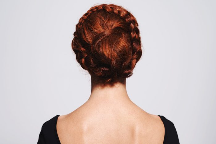 Studio shot of a redhead woman with a braided up-do posing against a gray background