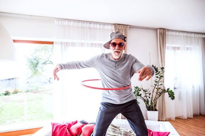 senior man using a hula hoop while standing on the couch in his home.