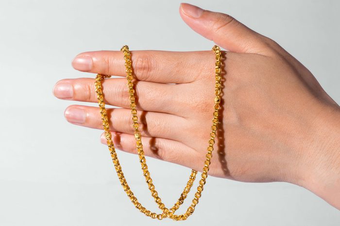 hand holding gold chain. gray background.