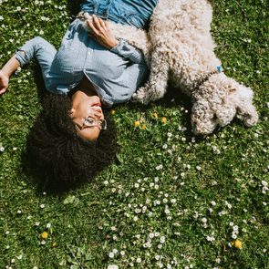 young woman lying on grass outside with her low maintenance white dog