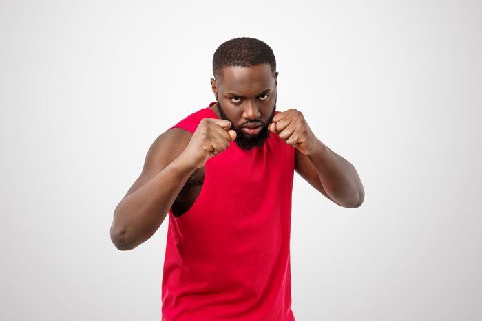 man in a red tank top holding his fists up like he is about to fight, studio shot against a gray background