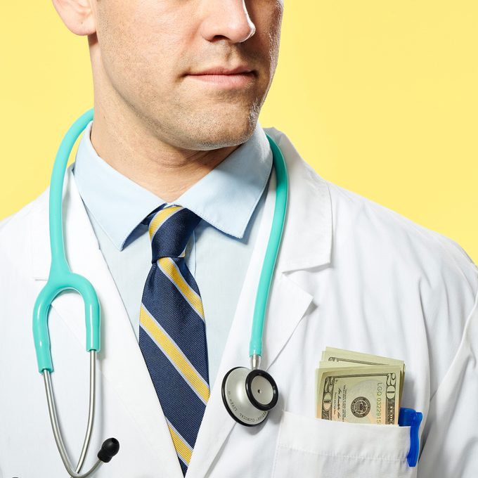 close up of doctor with money sticking out of his chest pocket. yellow background.