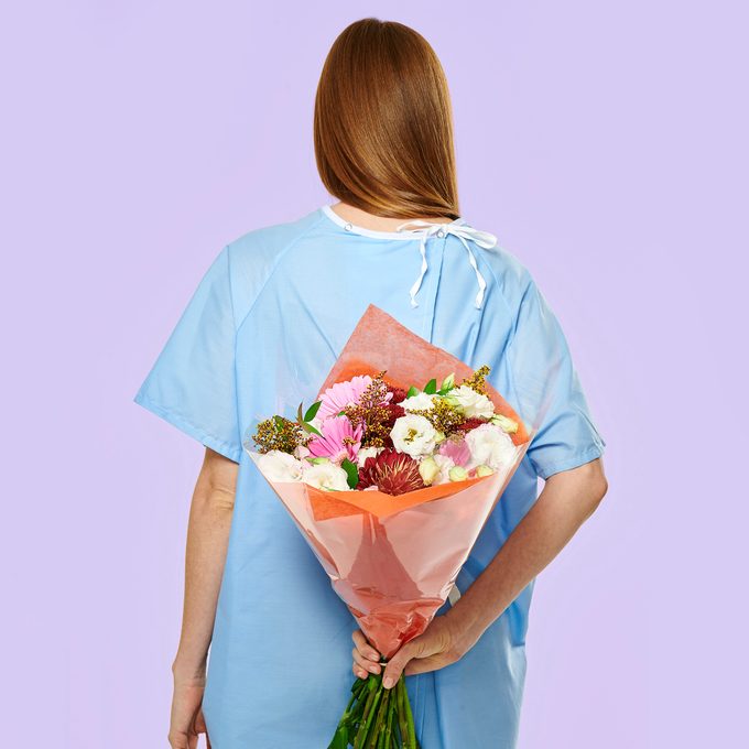 patient holding a bouquet of flowers behind her back. lavender background.