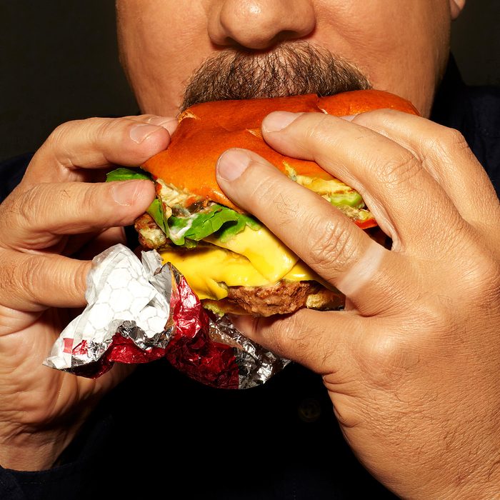 close up of man eating a fast food burger with wedding ring tan