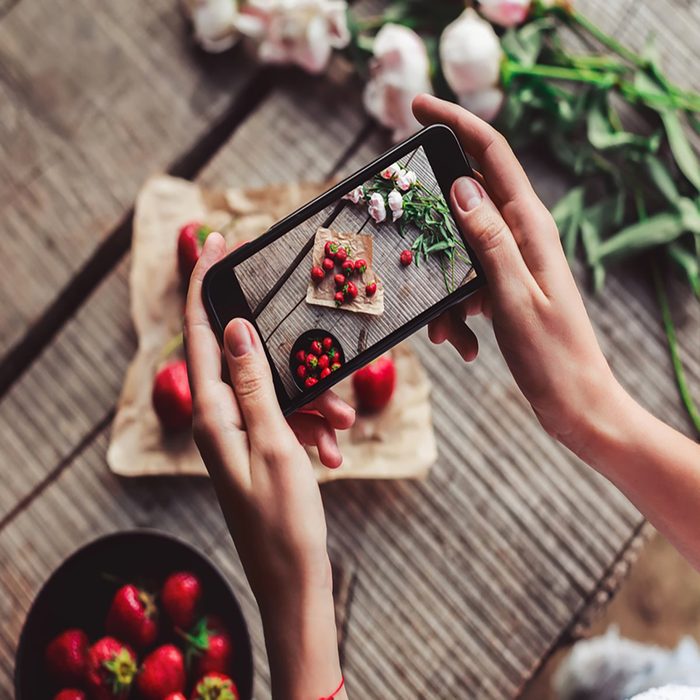 Girl's hands taking photo of breakfast with strawberries by smartphone. Healthy breakfast, Clean eating, vegan food concept.