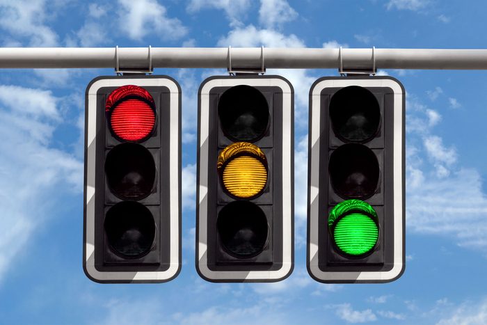 three Traffic Lights showing each of Red, Yellow, and Green colored lights Against Sky background