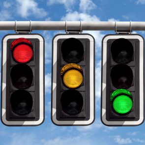 three Traffic Lights showing each of Red, Yellow, and Green colored lights Against Sky background