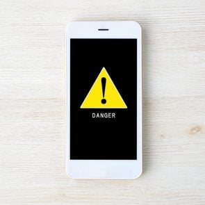 apple iphone virus warning; overhead view of a smartphone on a light wood background with an alert symbol on the screen
