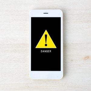 apple iphone virus warning; overhead view of a smartphone on a light wood background with an alert symbol on the screen