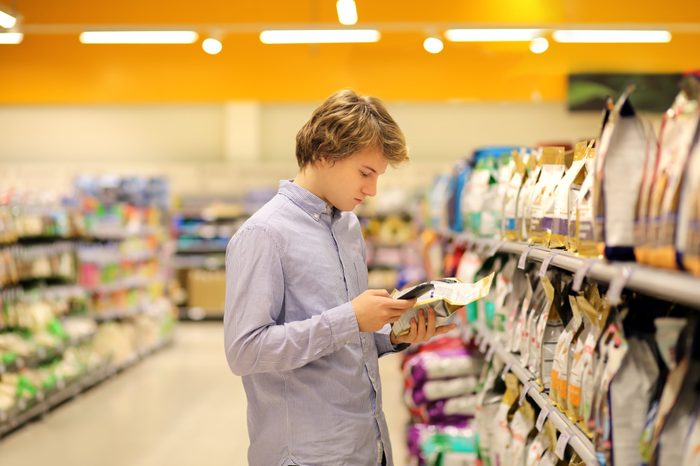 Man shopping in supermarket reading product information.Using smarthone.Pet food