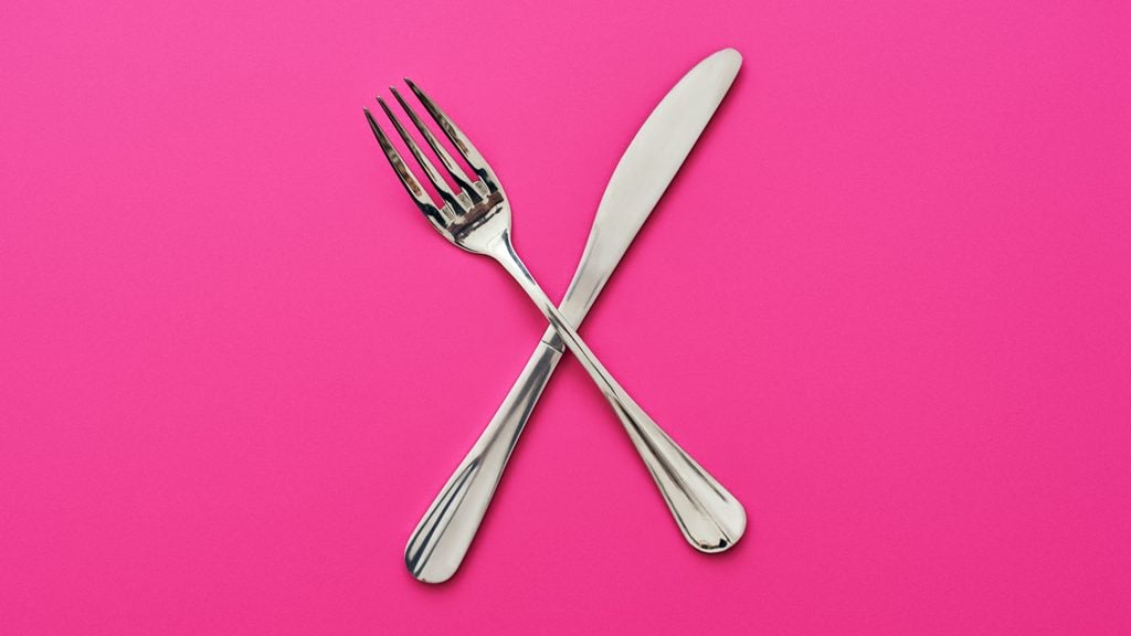 Knife and fork crossed, isolated on pink background